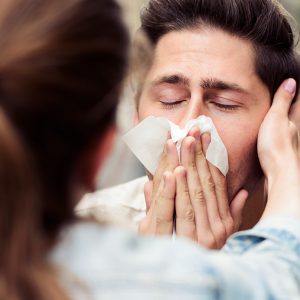 A kind woman looking after her suffering boyfriend as he blows his nose.